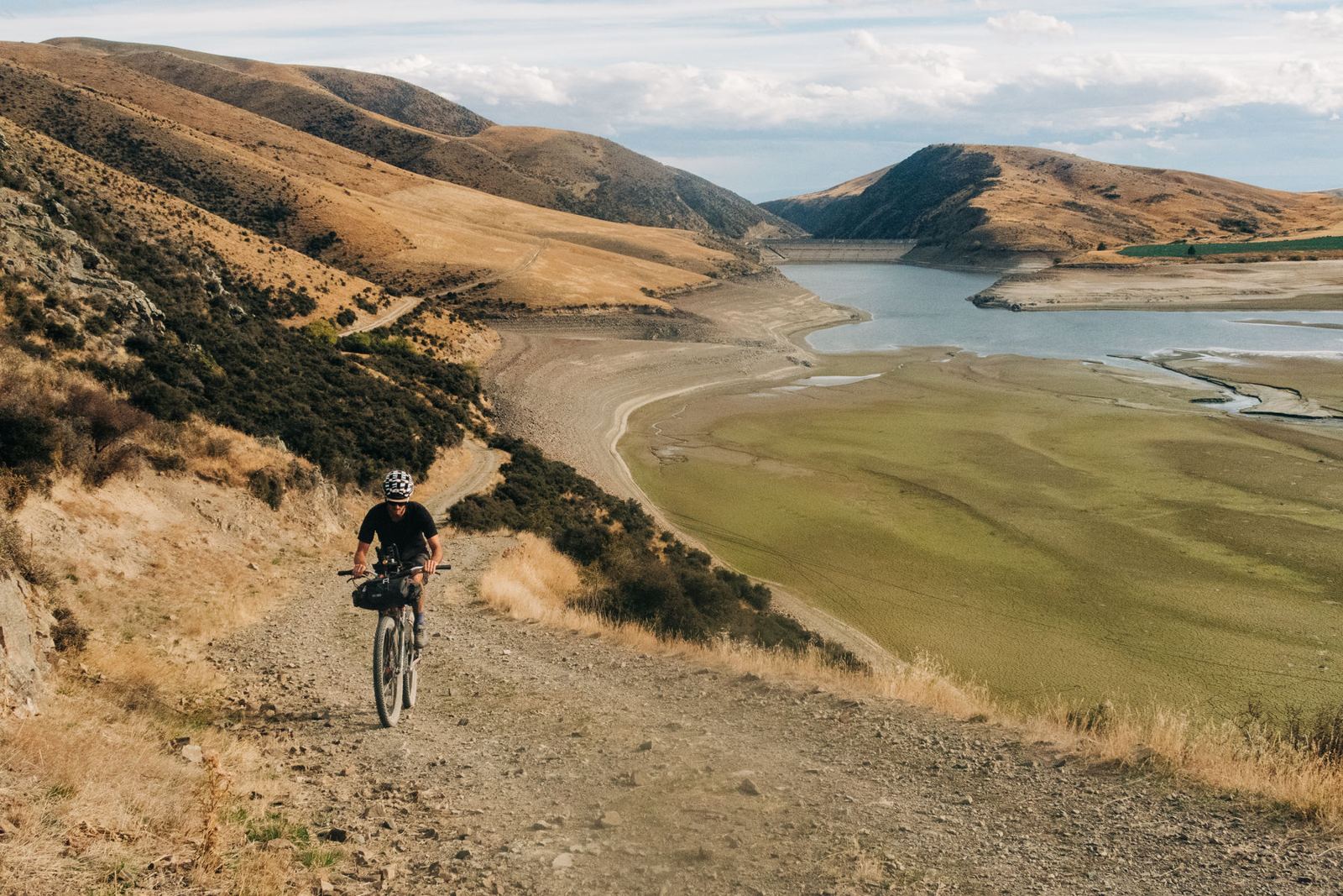 A rider descending a gravel track toward a lake