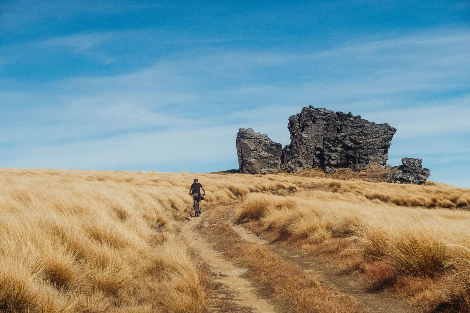 A rider on a tussock track below a schist tor